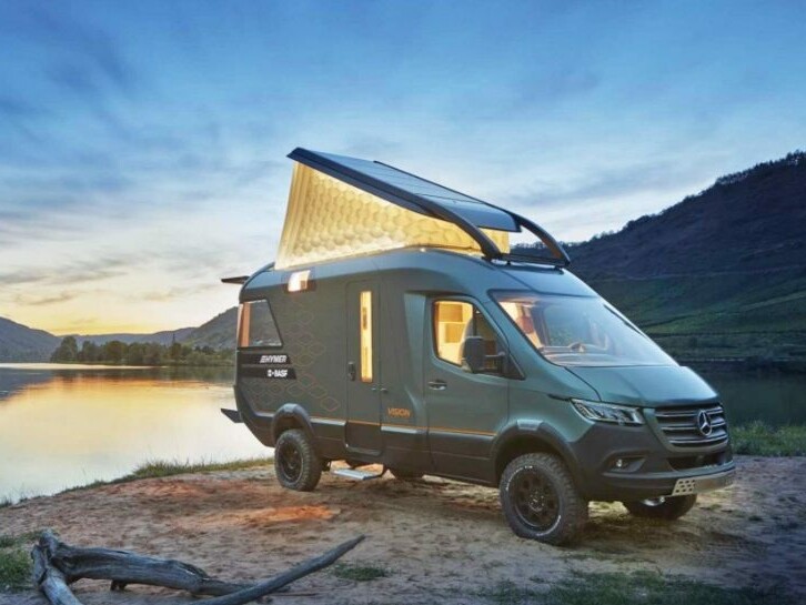 The Hymer VisionVenture campervan stands by a lake at dusk with the folding roof open.
