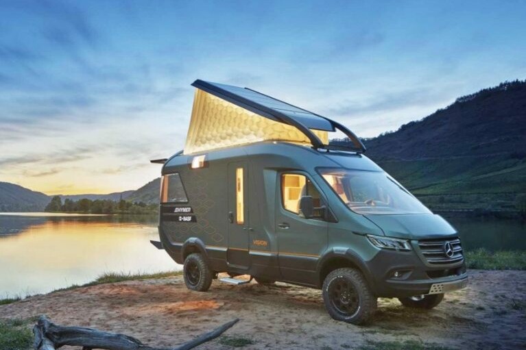 The Hymer VisionVenture campervan stands by a lake at dusk with the folding roof open.