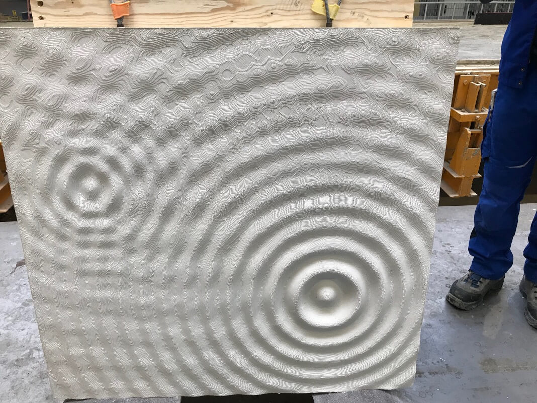 Light gray cast concrete facade panel shaped like spreading waves.