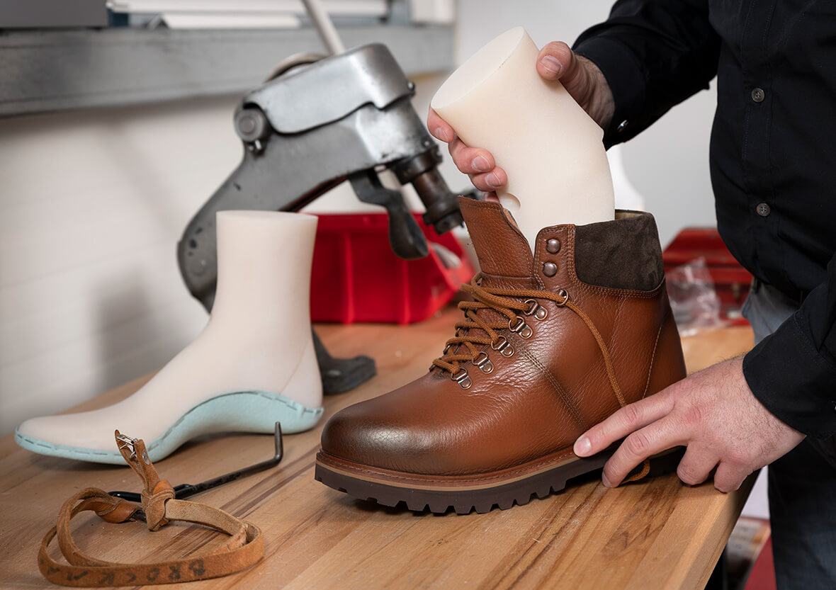 A countertop with a custom shoe last and the hands of a white man fitting a last into a brown leather orthopedic shoe.