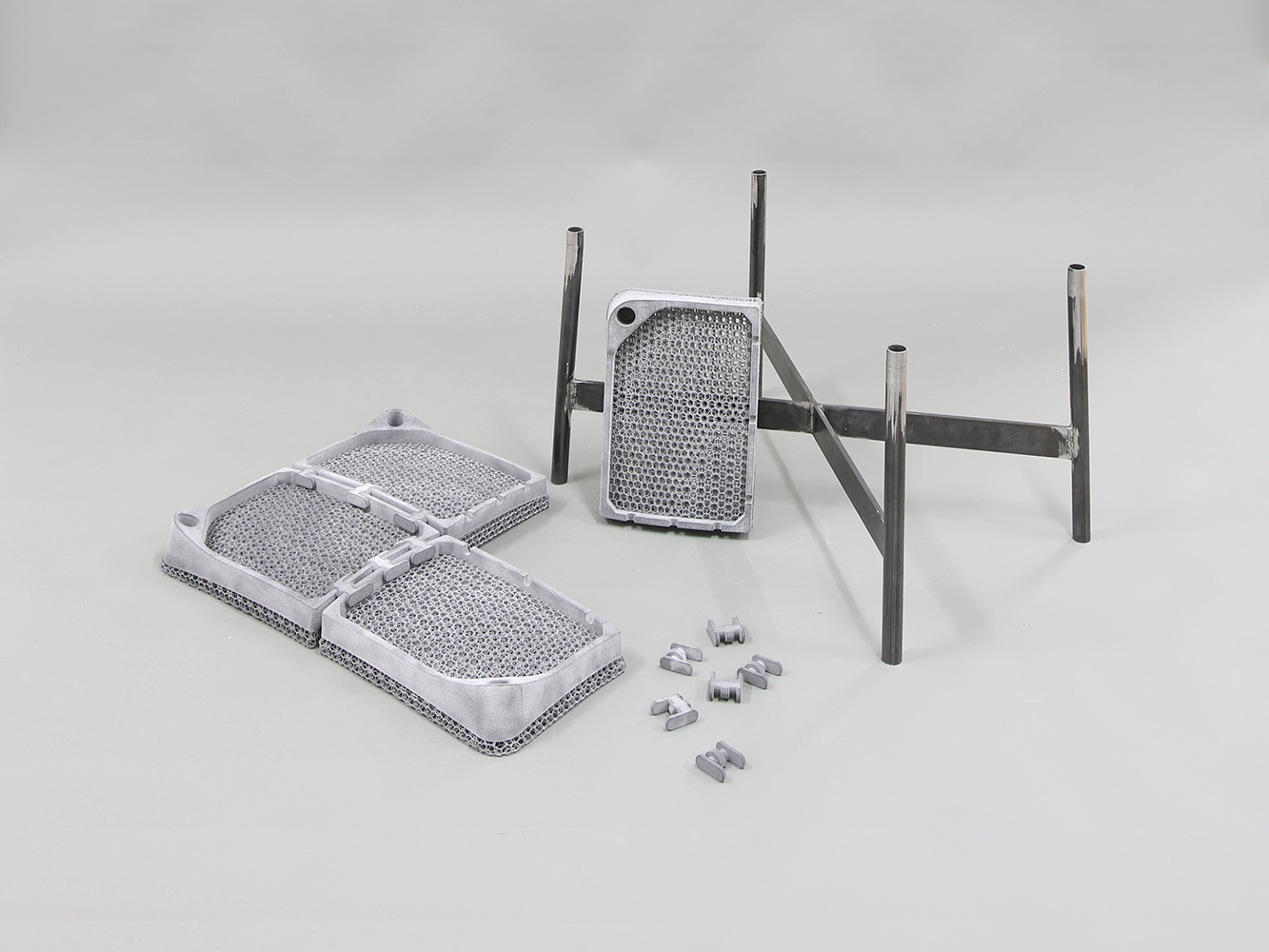 Metal substructure of a chair with a wide seat, individual components of the 3D-printed seat with a lattice structure lie on the floor in front of it.