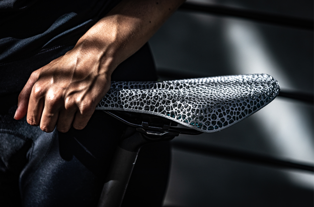 Close-up of a white woman's hand holding part of the grey 3D printed bicycle saddle with a custom lattice structure.